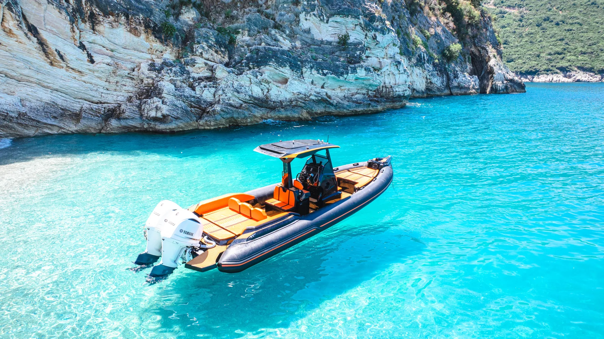 The Nemo Boat anchored under white cliffs in a clear turquoise cove on the Albanian Riviera