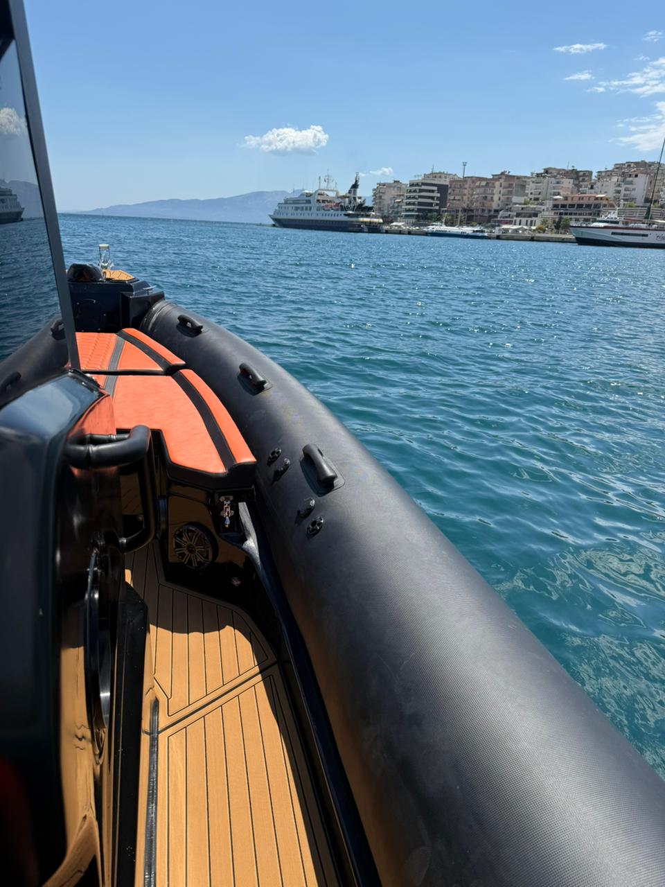 Teak deck and black tube on the Nemo Boat with Saranda port and a cruise ship in the distance